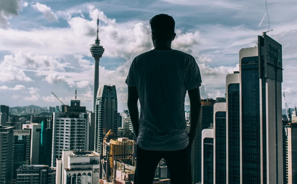 Home A silhouette of a man overlooking the Kuala Lumpur skyline, featuring the iconic KL Tower.